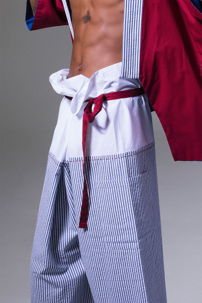 Model wearing Manda Thai Pants in pure cotton with relaxed unisex fit, vertical stripes, and red waist belt.