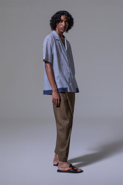 Model wearing Mosses Camp Shirt in pure cotton with vertical and horizontal stripe prints, open notch collar, clean button-up front, border applique at the hem, short sleeves, and side slits for a relaxed and characterful resort look.