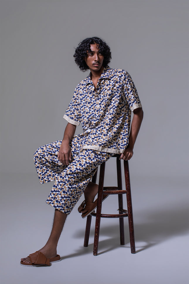 Model wearing Mordecoi Camp Shirt in lightweight cotton with geometric pattern, open notch collar, button-and-loop closure, contrast stripe borders, and side slits for a relaxed yet refined look.