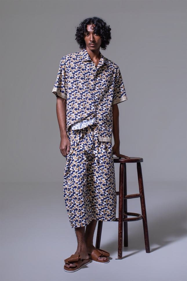 Model wearing Mordecoi Camp Shirt in lightweight cotton with geometric pattern, open notch collar, button-and-loop closure, contrast stripe borders, and side slits for a relaxed yet refined look.