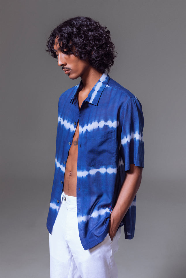 Model wearing Leon Camp Shirt in pure cotton with tie-dye stripe pattern, open notch collar, button-and-loop closure, clean button-up front, short sleeves, and side slits for a relaxed and serene warm-weather look.