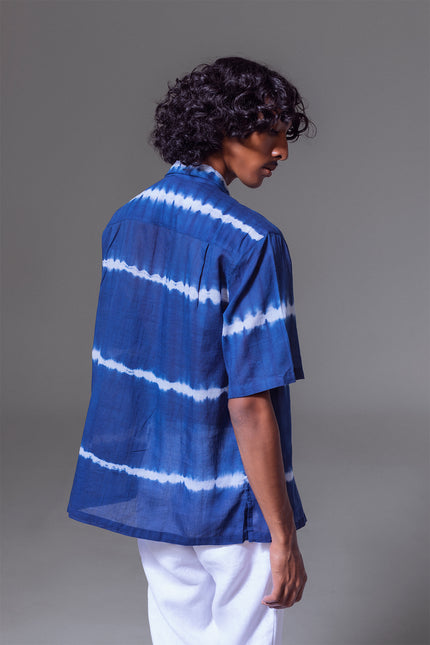 Model wearing Leon Camp Shirt in pure cotton with tie-dye stripe pattern, open notch collar, button-and-loop closure, clean button-up front, short sleeves, and side slits for a relaxed and serene warm-weather look.