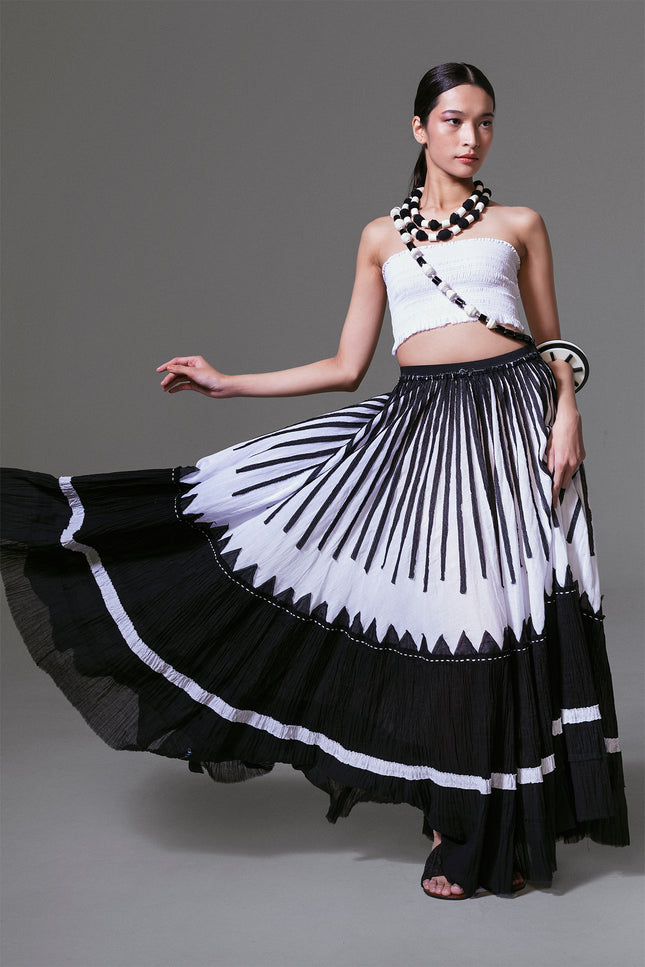 Model wearing black and white crinkled cotton maxi skirt with bold vertical appliqué, styled in flowing movement.