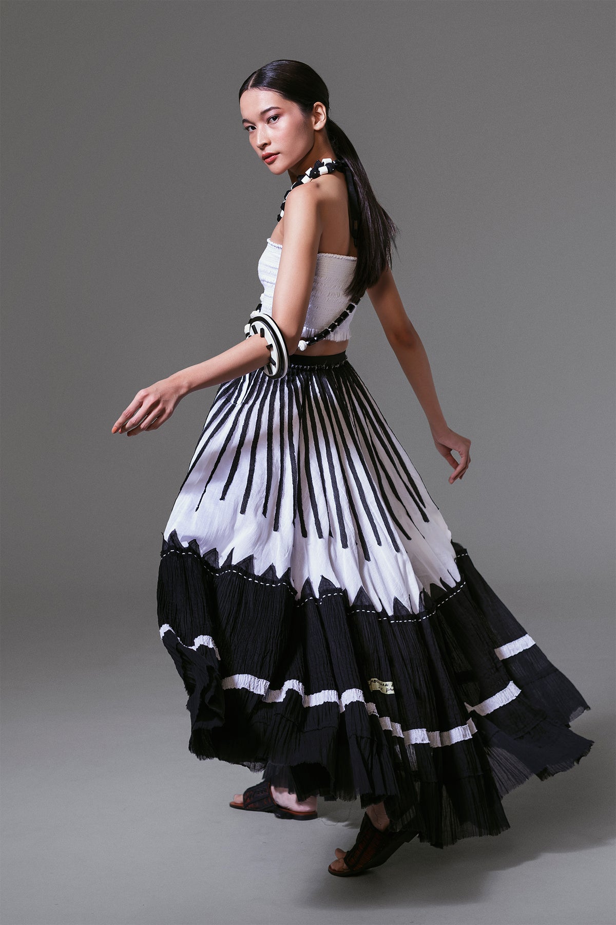 Model wearing black and white crinkled cotton maxi skirt with bold vertical appliqué, styled in flowing movement.