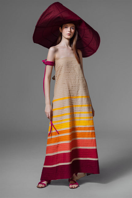 Model wearing long cotton dress with multicolor handcut stripe appliqué, open back, and tie strap detail.
