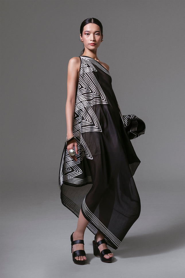 Model wearing black one-shoulder asymmetrical dress with white geometric ribbon appliqué and sheer silk-cotton finish.