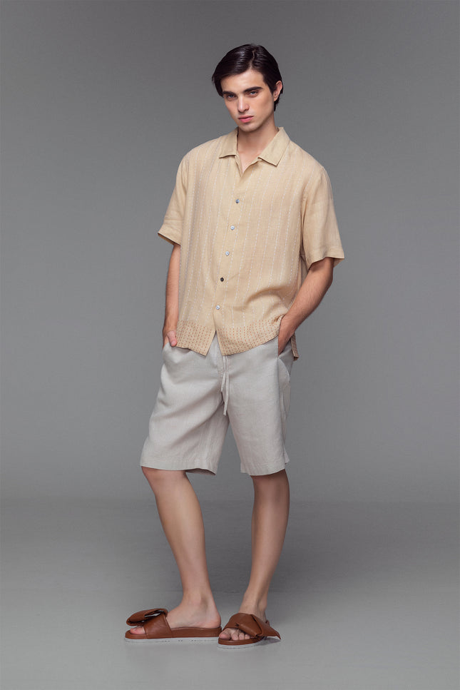 Model wearing stone-colored linen camp shirt with open collar, button front, and dual-colour hand-stitched detailing.