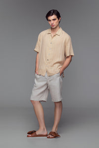 Model wearing stone-colored linen camp shirt with open collar, button front, and dual-colour hand-stitched detailing.