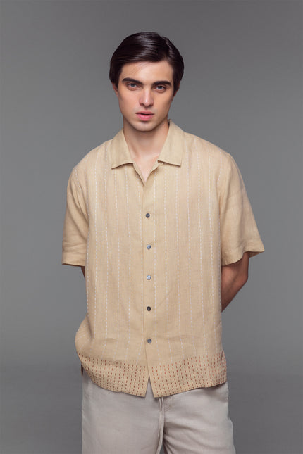 Model wearing stone-colored linen camp shirt with open collar, button front, and dual-colour hand-stitched detailing.
