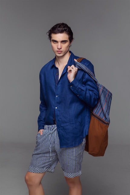 Model wearing reversible Mical Shorts in oriental blue and off-white blom print, featuring an elastic waistband with drawstrings, side and back pokets, and a short, breathable cotton silhouette for warm-weather wear.