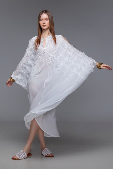 Model wearing white Magnolia Kaftan in sheer cotton with batwing silhouette, slit shoulders, and hand-stitched details.