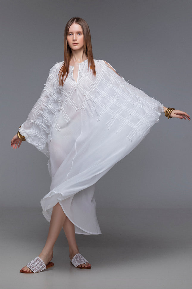 Model wearing white Magnolia Kaftan in sheer cotton with batwing silhouette, slit shoulders, and hand-stitched details.