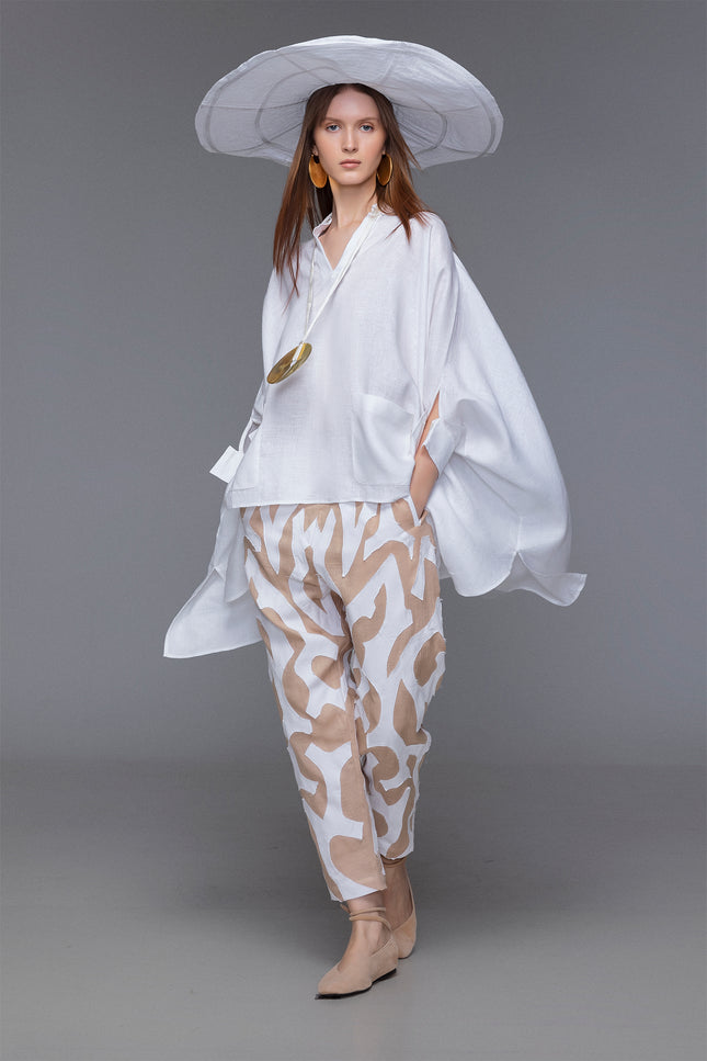 Model wearing Mason Pants with loose tapered silhouette, wide low crotch, contrasting tiger-like hand-cut appliqué, elastic waistband with inner drawstrings, and functional pokets for a relaxed yet refined resort look.
