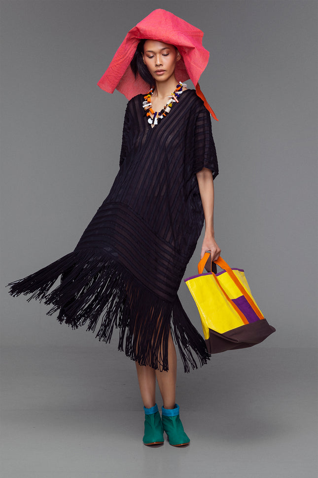Model wearing black cotton kaftan with handmade fringe and stripe appliqué, styled with bold accessories.