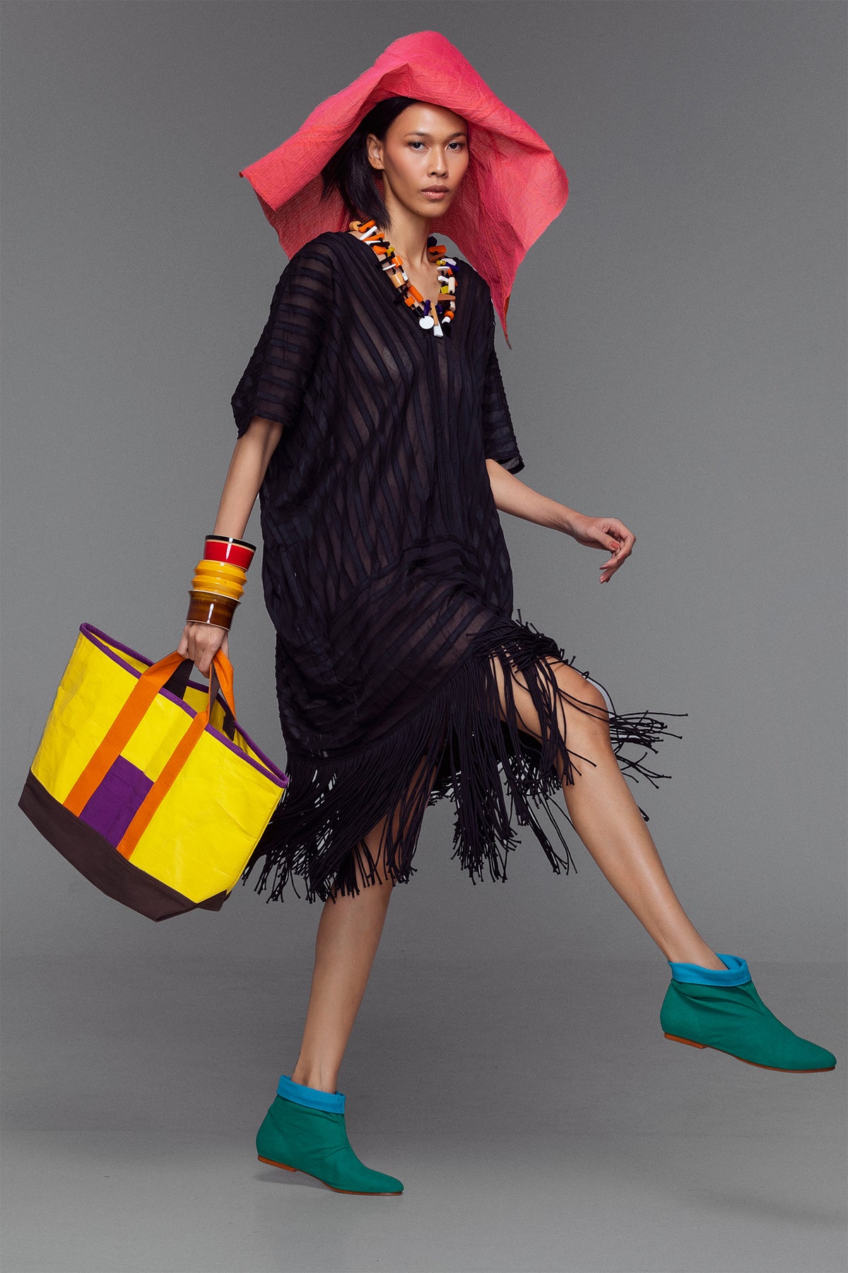 Model wearing black cotton kaftan with handmade fringe and stripe appliqué, styled with bold accessories.