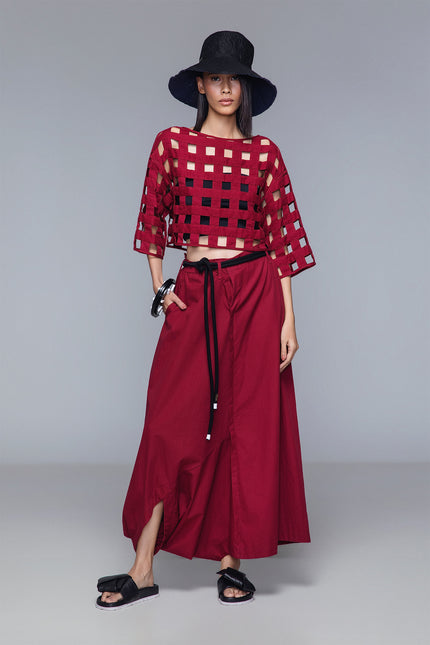 Asymmetrical draped skirt-pants in bordeaux, wide leg with fluid draping, shown on model.