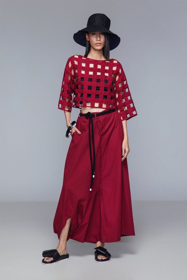 Asymmetrical draped skirt-pants in bordeaux, wide leg with fluid draping, shown on model.