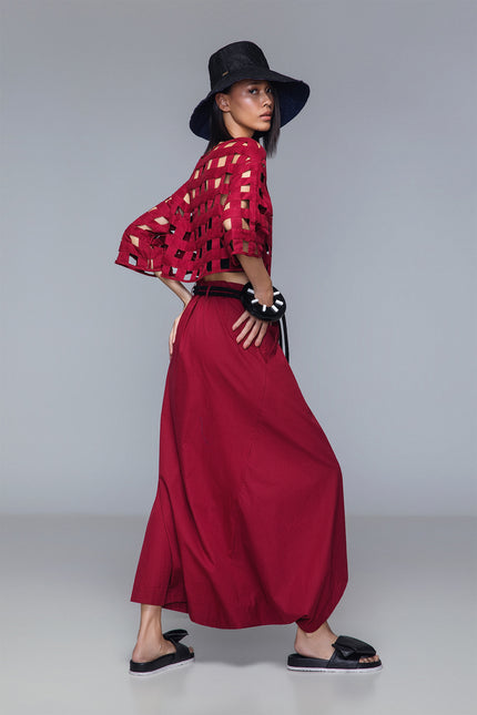 Asymmetrical draped skirt-pants in bordeaux, wide leg with fluid draping, shown on model.