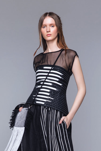Model wearing Matana Corset in pure cotton with adjustable back tail and strap closure, featuring monochrome ribbon detailing and contrast hand stitching for a refined statement look.