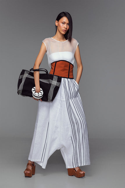 Model in white wide-leg trousers with Black ribbon appliqué, hand-stitched pleats, and cotton-linen texture.
