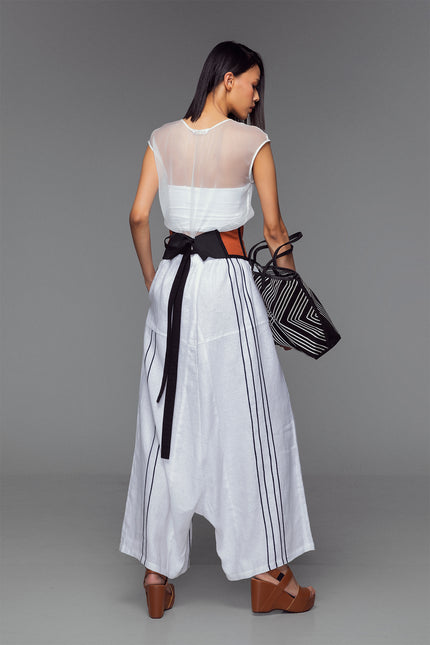Model in white wide-leg trousers with Black ribbon appliqué, hand-stitched pleats, and cotton-linen texture.
