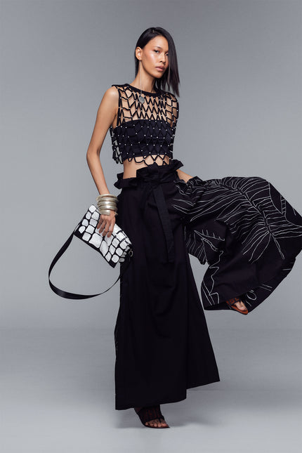 Model wearing Maliana Pants in pure cotton with a voluminous wide-leg silhouette, high-waist pleats, tropical flower embroidery, and a detachable belt for adjustable styling.