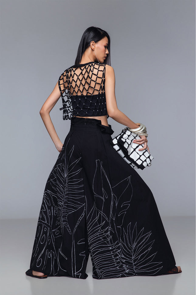 Model wearing Maliana Pants in pure cotton with a voluminous wide-leg silhouette, high-waist pleats, tropical flower embroidery, and a detachable belt for adjustable styling.