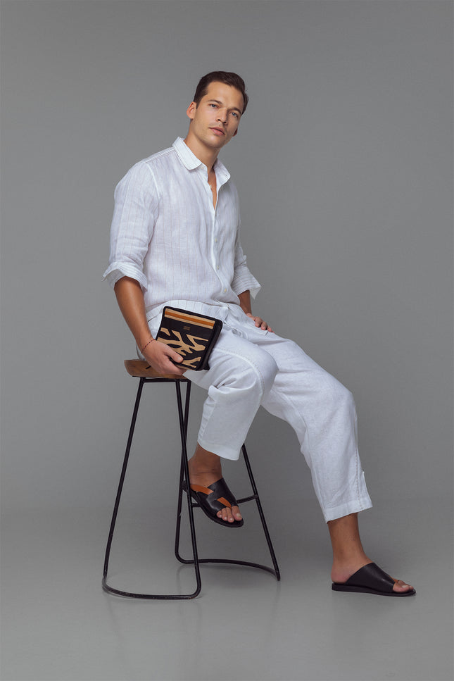 Model wearing white linen shirt with contrast stitching, long sleeves, and curved hemline, styled for a relaxed tailored look.