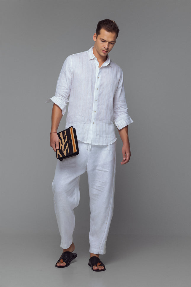 Model wearing white linen shirt with contrast stitching, long sleeves, and curved hemline, styled for a relaxed tailored look.