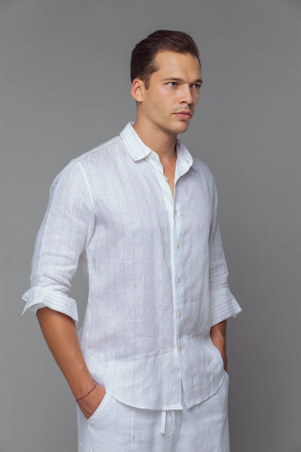 Model wearing white linen shirt with contrast stitching, long sleeves, and curved hemline, styled for a relaxed tailored look.