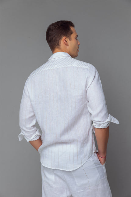 Model wearing white linen shirt with contrast stitching, long sleeves, and curved hemline, styled for a relaxed tailored look.