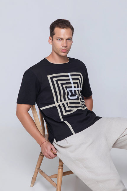Model wearing the Necho T-Shirt in lightweight cotton, featuring a bold labyrinth applique at the front, round neckline with subtle frill decoration, and short sleeves for breathable everyday style.