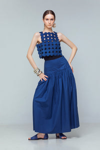Model wearing indigo linen crop top with coin-shaped appliqués, styled with a high-waisted gathered skirt.
