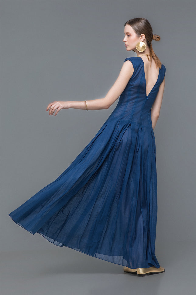 Model wearing Nadia Dress in an A-line silhouette with structured shoulders, boat neckline, and deep V back. Pleated detailing flows from the hip, crafted in a breathable ramie-cotton blend for refined summer occasions.