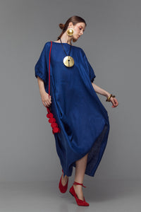 Model wearing indigo linen dress with ruffled sleeves, side drape detail, and left slit.
