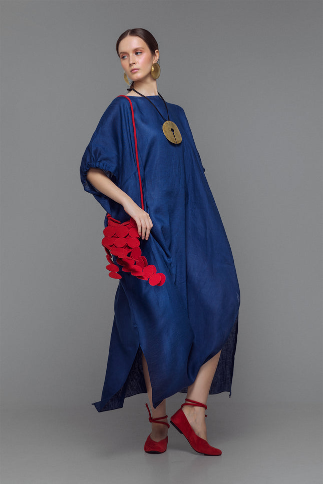 Model wearing indigo linen dress with ruffled sleeves, side drape detail, and left slit.
