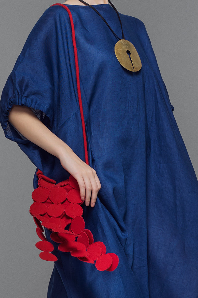 Model wearing a bold red Nysa Bag featuring coin applique detailing, an adjustable strap, and a magnetic snap closure, styled as a hands-free sling with playful dangling accents.