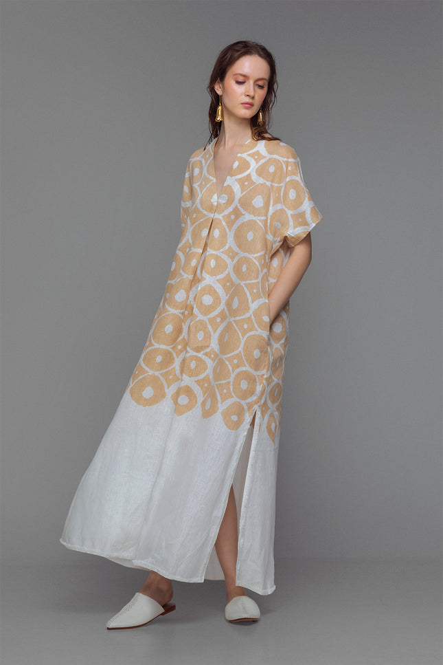 Model wearing beige and white kaftan with sun-inspired print, V-neck, and fringe detail at the slit.
