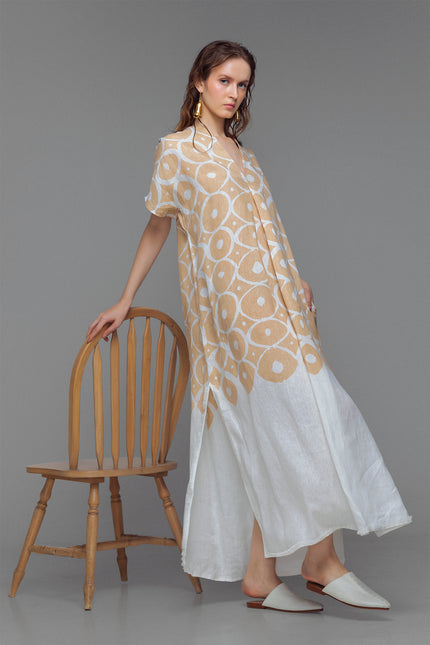 Model wearing beige and white kaftan with sun-inspired print, V-neck, and fringe detail at the slit.