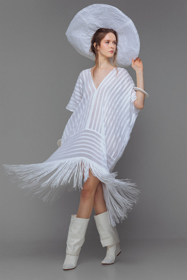 Model wearing white cotton kaftan with stripe appliqué and handmade fringe, styled for summer.