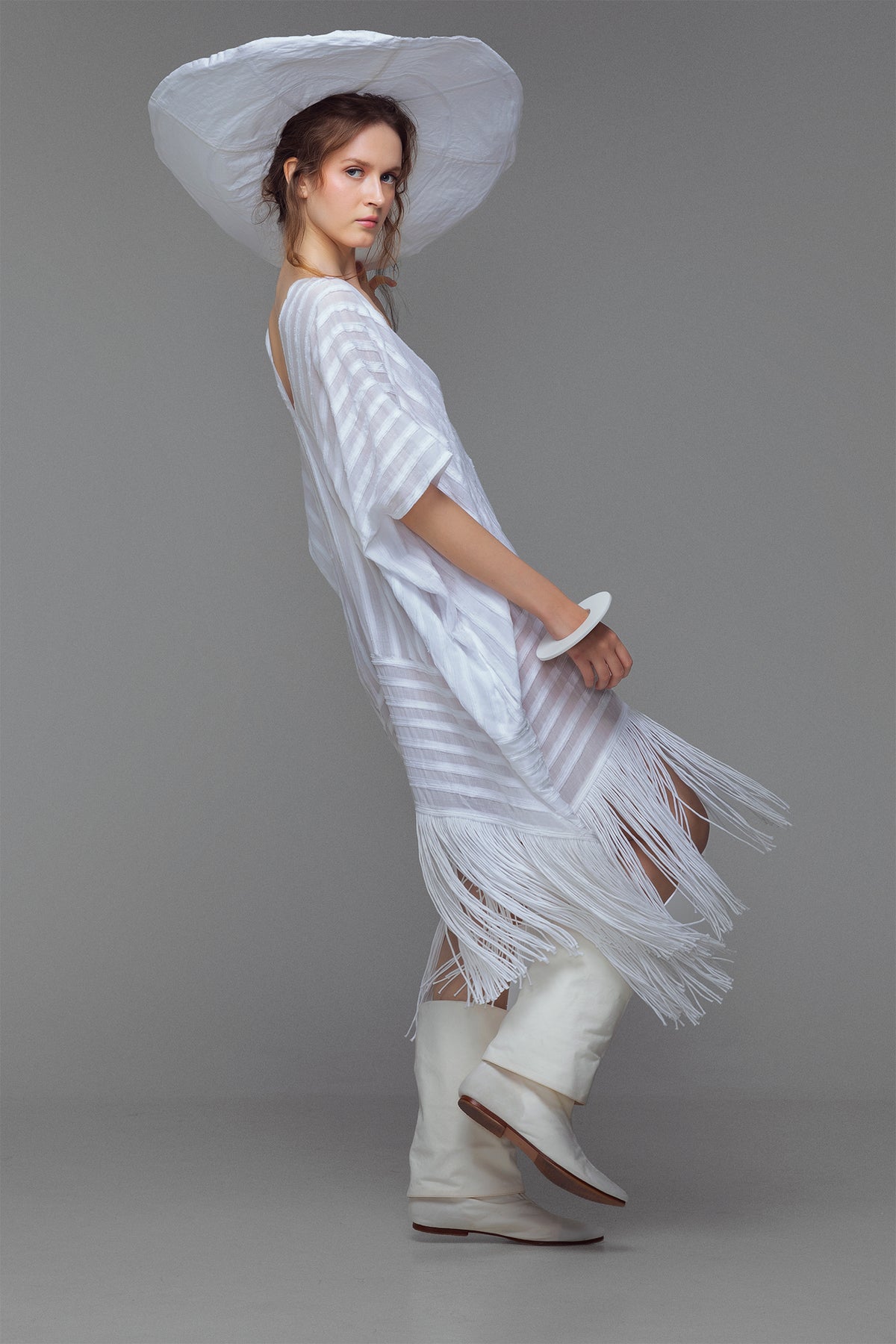 Model wearing white cotton kaftan with stripe appliqué and handmade fringe, styled for summer.