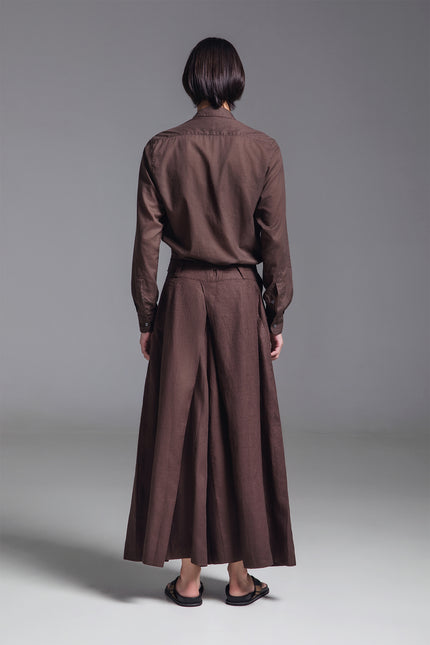 Model wearing wide pleated linen pants with deep front pleats, side zipper, and fixed waist belt detail.