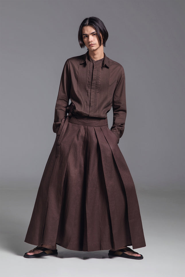 Model wearing wide pleated linen pants with deep front pleats, side zipper, and fixed waist belt detail.