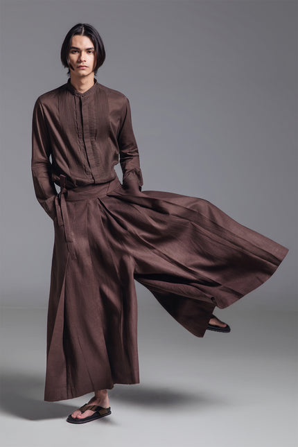 Model wearing wide pleated linen pants with deep front pleats, side zipper, and fixed waist belt detail.