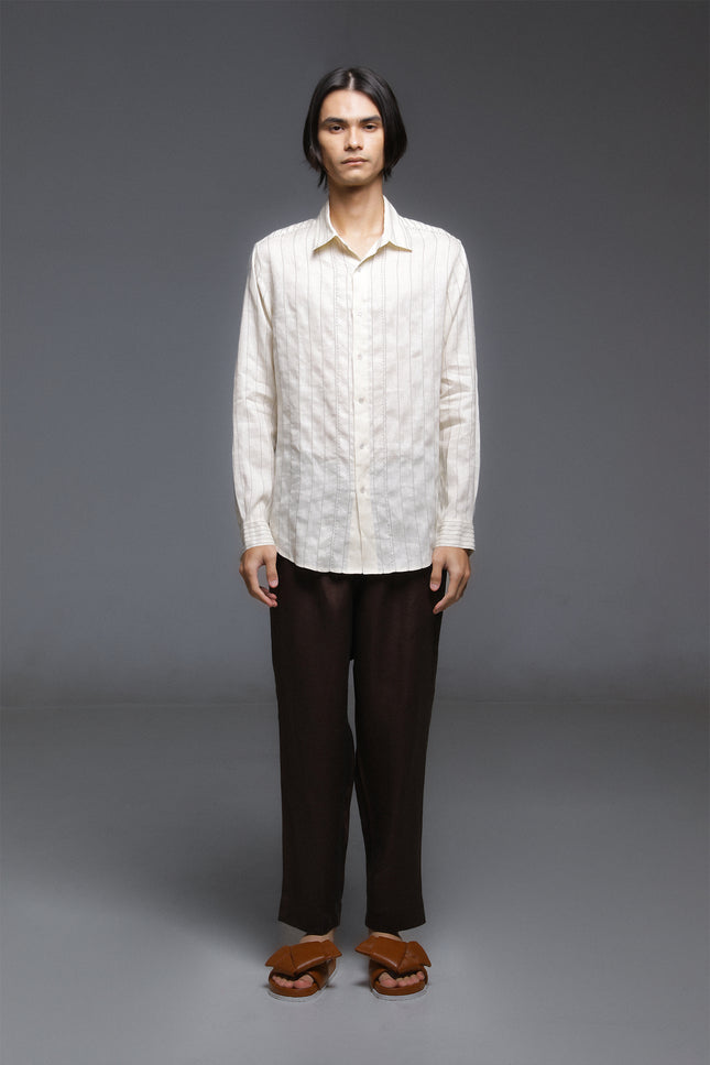 Model wearing white linen shirt with contrast stitching, long sleeves, and curved hemline, styled for a relaxed tailored look.