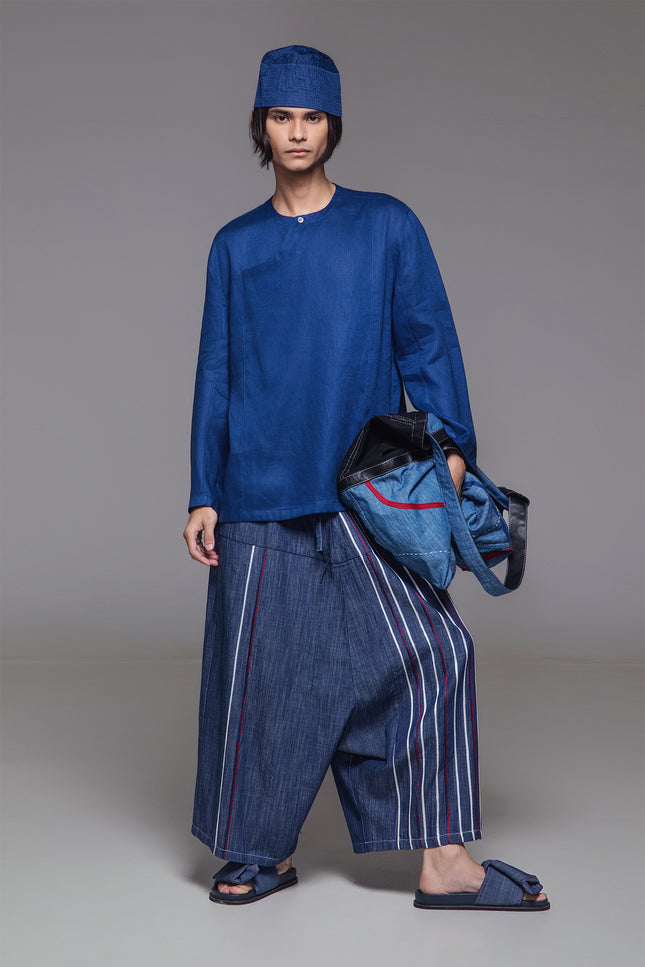 Model wearing indigo drop-crotch pants with multicolor ribbon appliqué and elastic drawstring waist.
