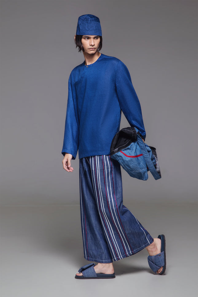 Model wearing indigo drop-crotch pants with multicolor ribbon appliqué and elastic drawstring waist.
