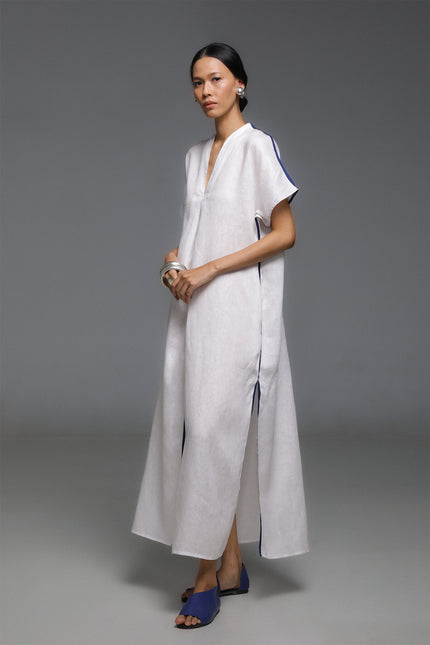 Model wearing Odis Kaftan in pure linen, featuring a loose silhouette with clean lines, V-neckline, side slit, contrast binding, and neutral palette, perfect for a relaxed resort wear.