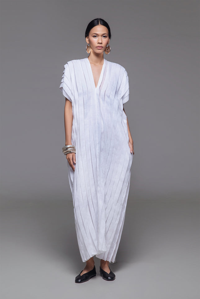 Model wearing Naria Kaftan in light cotton with floor-length straight silhouette, full vertical pleats, and V-neckline for a clean, architectural look.