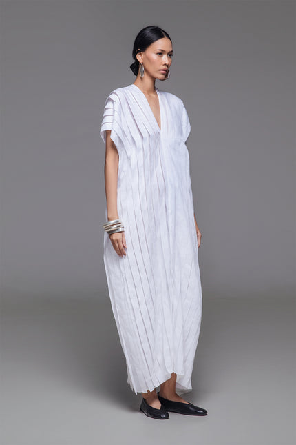 Model wearing Naria Kaftan in light cotton with floor-length straight silhouette, full vertical pleats, and V-neckline for a clean, architectural look.